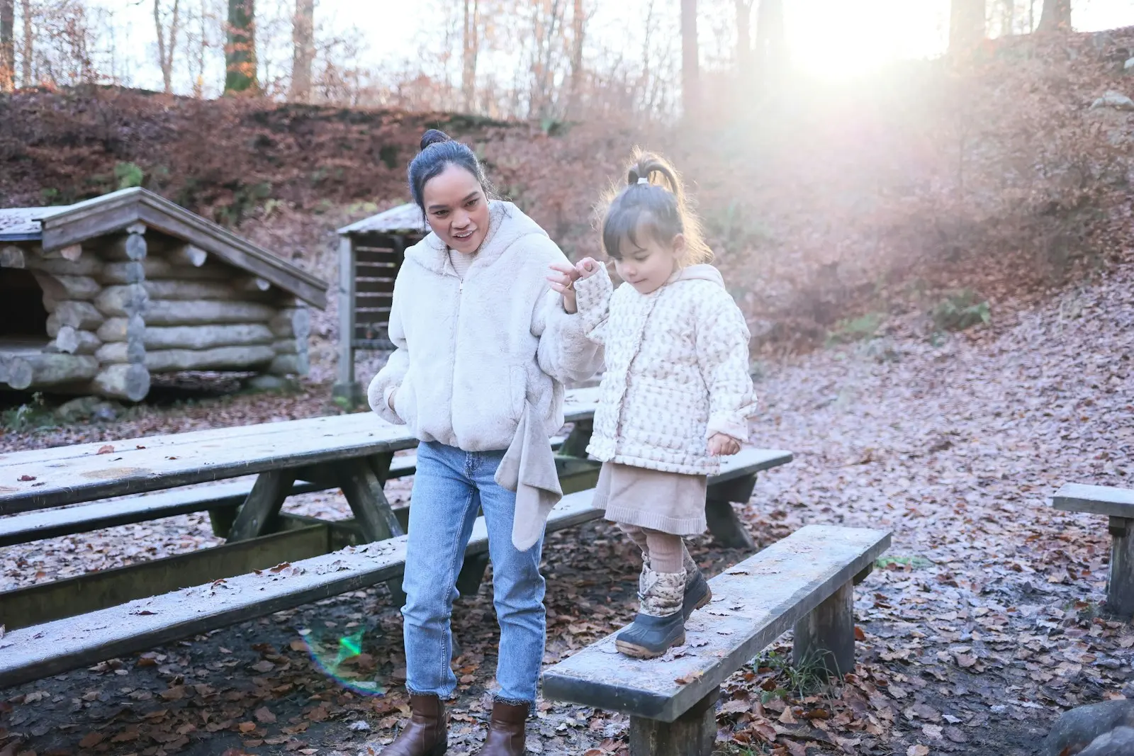 A woman steadying a young child walking along a park bench